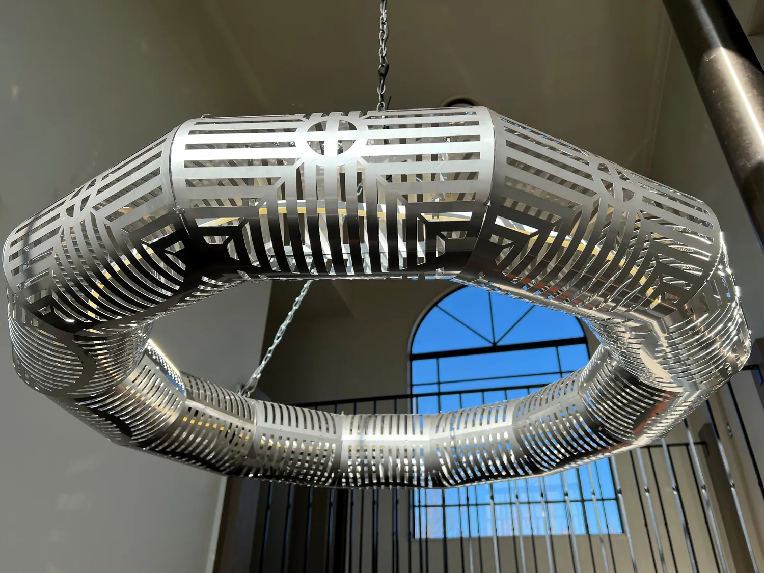 Positive Earth laser-cut sculptural ring light in polished metal with a geometric pattern.